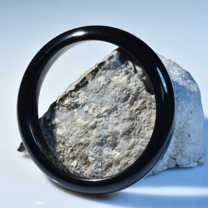 May include: A black jade bangle bracelet, resting on a rough, gray stone.
