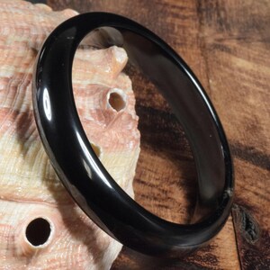 Op de afbeelding: Een zwarte bangle-armband gemaakt van gepolijst, glad, glanzend materiaal. De armband is dik en breed, met een afgeronde rand.