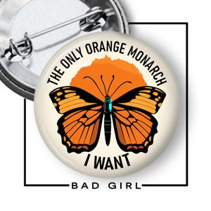 May include: A round button pin with a monarch butterfly design. The butterfly is orange and black with a blue center. The text on the button reads "THE ONLY ORANGE MONARCH I WANT BAD GIRL."