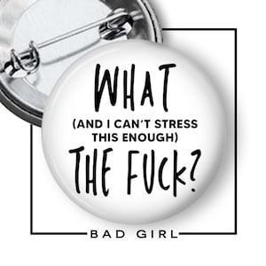 May include: A white button with the text "WHAT (AND I CAN'T STRESS THIS ENOUGH) THE FUCK?" in black. The words "BAD GIRL" are at the bottom. The button has a metal pin back.