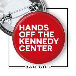 May include: A round red pin-back button featuring the white text HANDS OFF THE KENNEDY CENTER. The back of the button is metallic silver with a pin mechanism. Below the button, the text BAD GIRL is printed in black within a square frame.