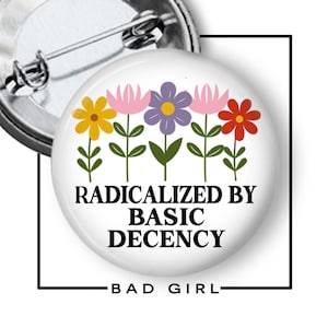 May include: A white button pin with a floral design and the text "RADICALIZED BY BASIC DECENCY". The pin features a metal clasp and the words "BAD GIRL" at the bottom.