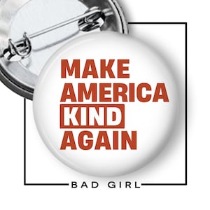 May include: A round pinback button with a white background and rust-colored text that reads MAKE AMERICA KIND AGAIN. The word KIND is inside a rust-colored rectangular box. The back of the button features a silver metal pin mechanism.