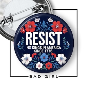 May include: A round, navy blue button with the word "RESIST" in white, surrounded by red, white, and blue floral designs. The text "NO KINGS IN AMERICA SINCE 1776" is below the main text. The words "BAD GIRL" are at the bottom.