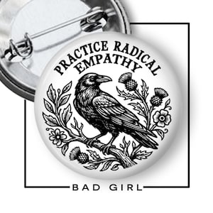 May include: A circular pin-back button featuring a black and white illustration of a raven perched on a branch surrounded by thistle flowers. The text "PRACTICE RADICAL EMPATHY" is printed in a black serif font in an arc above the raven.