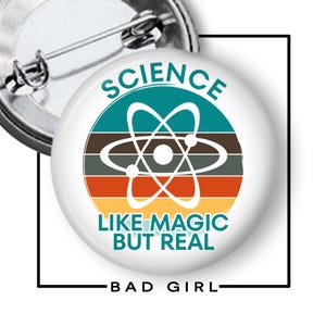 May include: A round pin-back button featuring a white background with a central graphic of an atom symbol over horizontal stripes in teal, brown, orange, and yellow. The text reads SCIENCE LIKE MAGIC BUT REAL in teal capital letters.