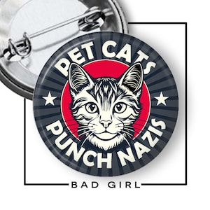 May include: A round button with a cat illustration and the text "PET CATS PUNCH NAZIS". The design features a cat's face in the center, surrounded by text and stars. The words "BAD GIRL" are at the bottom.