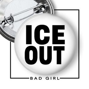 May include: A circular pin-back button featuring a white background with the bold black text ICE OUT centered on the front. The back of the button is metallic silver with a pin mechanism. Below the button, the text BAD GIRL is printed in black.