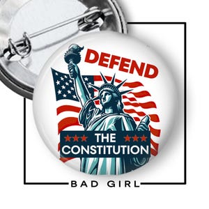 May include: A round button pin featuring the Statue of Liberty holding a torch, with the American flag in the background. The words "DEFEND THE CONSTITUTION" are displayed in red and blue. The text "BAD GIRL" is at the bottom.
