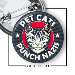 May include: A circular pin-back button featuring a graphic of a cat face centered over a red circle. The background has dark gray radiating stripes. The text PET CATS PUNCH NAZIS is printed in white capital letters around the cat. A metal pin is visible.