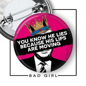 May include: A round button with a pink background and the text "YOU KNOW HE LIES BECAUSE HIS LIPS ARE MOVING" in white. The button features a graphic of a person wearing a crown. The words "BAD GIRL" are at the bottom.