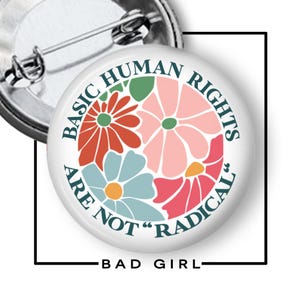May include: A white button pin with the text "BASIC HUMAN RIGHTS ARE NOT 'RADICAL'" encircling a floral design in shades of pink, orange, blue, and green. The pin has a metal backing and the words "BAD GIRL" are at the bottom.