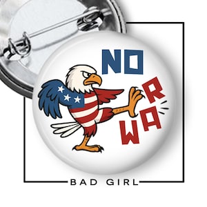 May include: A white button pin featuring a cartoon eagle with the American flag design kicking the letters "R" and "WA". The words "NO" and "BAD GIRL" are also displayed on the pin.