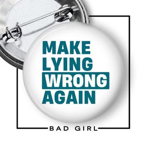 May include: A round white pin-back button featuring the dark teal text "MAKE LYING WRONG AGAIN" with the word "WRONG" highlighted in a solid dark teal rectangular block. The back of the button shows a silver metal pin mechanism for attachment.