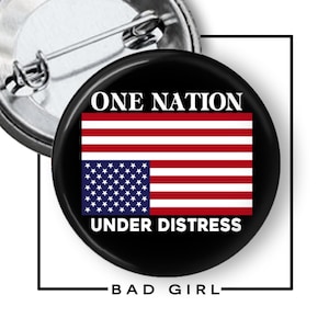 May include: A circular pin-back button featuring a black background with the white text ONE NATION at the top and UNDER DISTRESS at the bottom. Centered is an inverted American flag with the blue field of stars positioned at the bottom left.