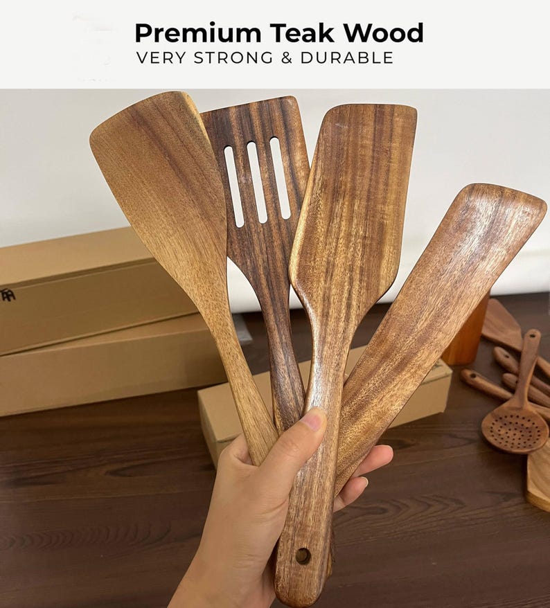 Może przedstawiać: Kolekcja drewnianych przybor&oacute;w kuchennych, w tym szpatułek i łyżek szczelinowych, wykonanych z wysokiej jakości drewna tekowego. Przybory mają ciepły brązowy kolor z widocznym usłojeniem drewna.