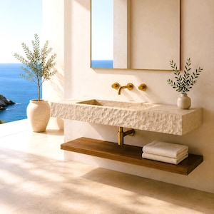 May include: A modern bathroom with a stone sink, brass fixtures, and a wooden shelf. A rectangular mirror hangs above the sink. A small plant in a vase and a potted tree add a natural touch. The ocean is visible in the background.