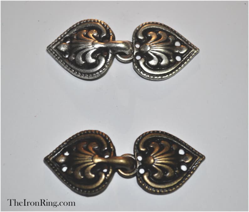 May include: Two heart-shaped metal clasps, one silver and one gold, with intricate floral designs. The clasps are designed to be used as a closure for garments or accessories.