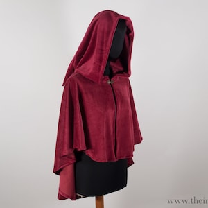 以下が含まれることがあります： ボタン留めのシングルフード付きのワインレッドのケープ。ケープは柔らかく、豪華な生地で作られています。