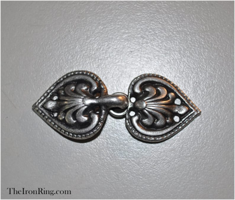 May include: A silver-toned metal clasp with a heart-shaped design. The clasp has intricate details and a decorative flourish in the center.
