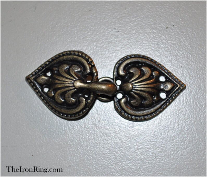 May include: A pair of ornate, heart-shaped metal clasps with a decorative floral design. The clasps are a dark bronze color and have a hook and loop closure.