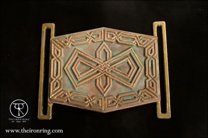May include: A decorative metal belt buckle with a geometric design in shades of copper and green. The buckle has a rectangular shape with two loops on either side.