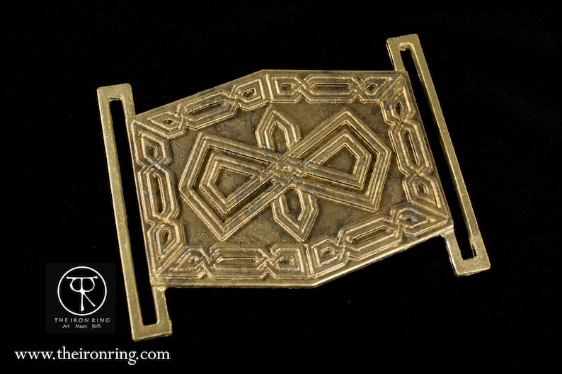 May include: A gold-toned metal belt buckle with an intricate geometric design. The buckle features a repeating pattern of squares and diamonds.