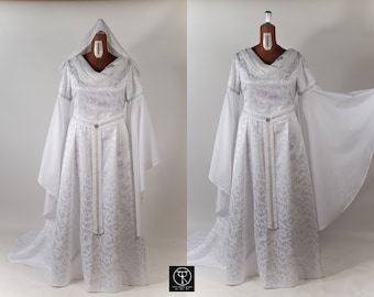 Puede incluir: Un vestido blanco con una larga cola y un cinturón plateado. El vestido tiene un corpiño ajustado y mangas largas con un diseño amplio y fluido. El vestido está hecho de una tela de brocado con un patrón floral.