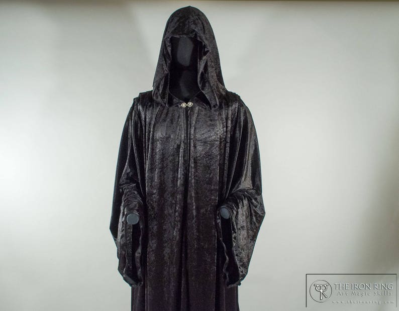 May include: A black velvet hooded robe with a long, flowing design. The robe has a silver clasp at the neck and two pockets on the front.
