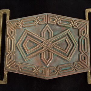 May include: A bronze belt buckle with a geometric design. The buckle has a green patina and is decorated with intricate patterns.