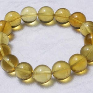 Puede incluir: Un brazalete hecho de cuentas redondas de color ámbar. Las cuentas son todas del mismo tamaño y están enhebradas en un cordón elástico transparente.