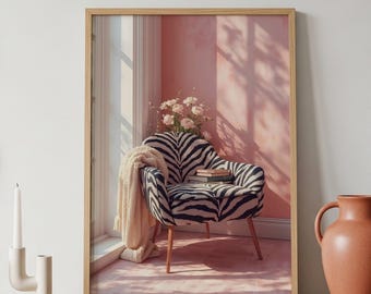 May include: A framed print featuring a zebra-print armchair with wooden legs. A cream-colored throw blanket and books rest on the chair. The background includes a pink wall, a window, and a vase of flowers, creating a cozy interior scene.