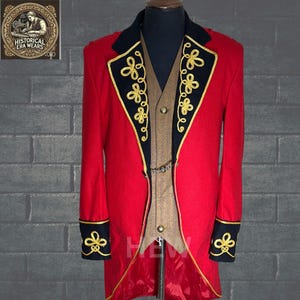 Puede incluir: Una chaqueta roja de manga larga con ribetes negros y bordados dorados. La chaqueta tiene un cuello alto y un cierre de un solo botón. La chaqueta se lleva sobre un chaleco marrón.
