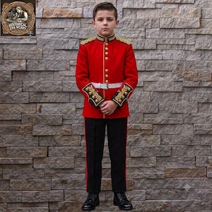 May include: A child wearing a bright red military-style tunic with gold embroidery on the shoulders and cuffs, featuring gold buttons, a white belt with a silver buckle, and black trousers with a thin red stripe down the side, paired with black shoes.