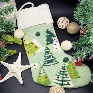 Könnte beinhalten: Ein grüner Filz-Weihnachtsstrumpf mit weißem Bündchen, verziert mit gestickten grünen Weihnachtsbäumen und roten Beeren.