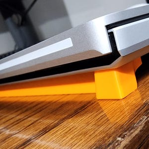 May include: A silver laptop computer is raised on two orange plastic stands. The laptop is on a wooden surface.