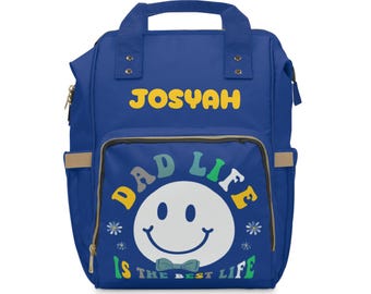 May include: Blue diaper bag backpack with the text "JOSYAH" on the top flap and "DAD LIFE IS THE BEST LIFE" with a smiley face on the front.