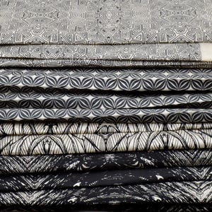 May include: A stack of fabric swatches with black and white geometric patterns. The patterns include a repeating flower design, a geometric design with squares and diamonds, and a design with a series of lines.