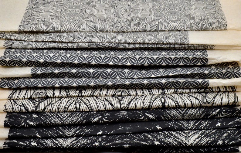 May include: A stack of fabric swatches with black and white geometric patterns. The patterns include a repeating flower design, a geometric design with squares and diamonds, and a design with a series of lines.