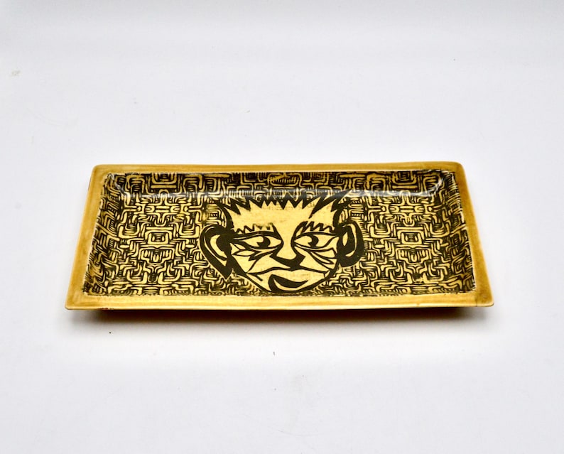 May include: A rectangular ceramic tray with a black and white graphic of a face on a yellow background. The face has a black outline and a black and white patterned background.