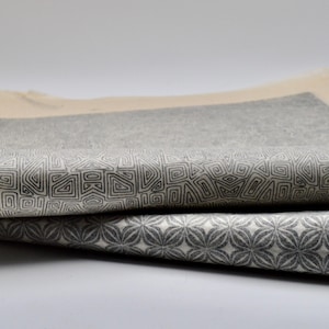 May include: Two pieces of fabric with geometric patterns printed on them. The top fabric has a pattern of small squares and the bottom fabric has a pattern of small flowers.