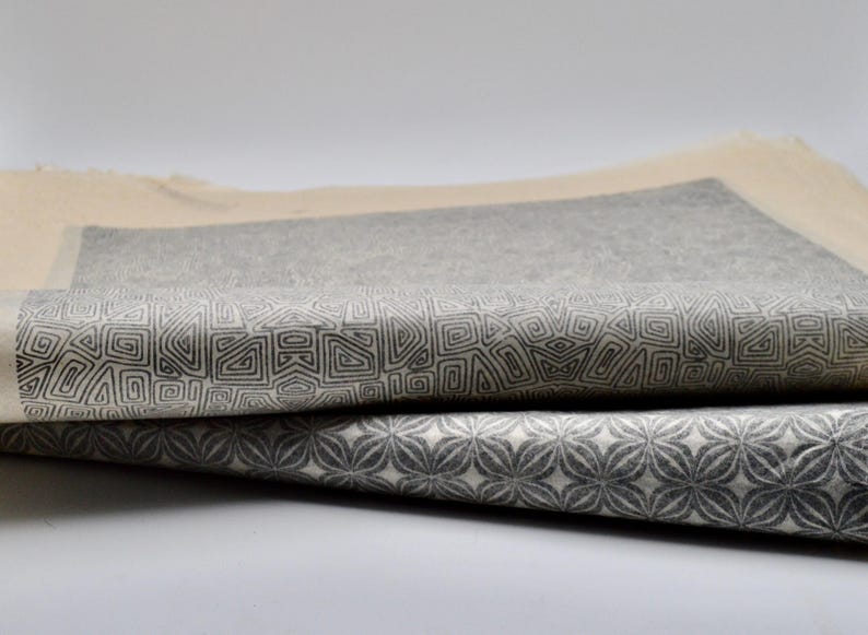 May include: Two pieces of fabric with geometric patterns printed on them. The top fabric has a pattern of small squares and the bottom fabric has a pattern of small flowers.