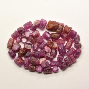 May include: A collection of small, rough, pink and red ruby crystals. The crystals are various shapes and sizes, and have a natural, unpolished look.