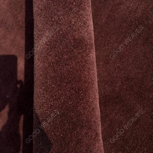 May include: A dark brown, plush, textured fabric surface with a folded edge. The text GOOD WEAVES is visible in multiple locations across the material, indicating the brand name on this deep brown, soft, and dense textile material.