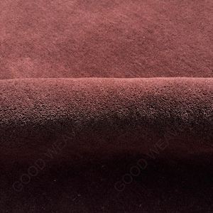 May include: Close-up of a section of claret-coloured fabric with a soft, velvety texture. The fabric is folded over, revealing a darker shade of the same colour underneath. The words "GOOD WEAVE" are partially visible.