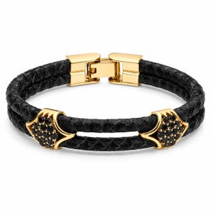 Può includere: Un bracciale a doppio filo in pelle nera testurizzata con dettagli in metallo dorato. Due elementi geometrici dorati sono incastonati con piccole pietre nere. Il bracciale include una chiusura in metallo dorato nella parte superiore.