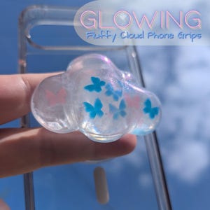 May include: A clear, cloud-shaped phone grip with blue and pink butterfly accents. The grip is filled with iridescent glitter and the text "GLOWING Fluffy Cloud Phone Grips" is visible in the background.