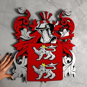 Puede incluir: Escudo familiar decorativo de madera en rojo, plata y negro. El escudo presenta un yelmo, dos leones y adornos ornamentales. El fondo es gris claro.