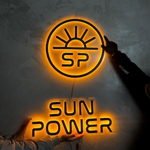 May include: Illuminated neon sign with the words "SUN POWER" and a circular logo featuring a sun design and the letters "SP". The sign emits a warm orange glow against a gray wall.