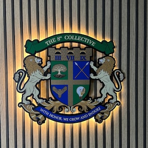 Könnte beinhalten: Ein dekoratives Emblem mit einem Wappen mit einem Baum, gekreuzten Speeren, einer Eule und einer Glühbirne. Zwei Löwen flankieren das Wappen, und der Text "THE 8TH COLLECTIVE" wird darüber angezeigt. Das Emblem enthält auch den Text "WITH HONOR, WE GROW AND ENDURE".